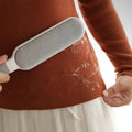 Person using a pet hair remover on a sweater with visible pet hair.