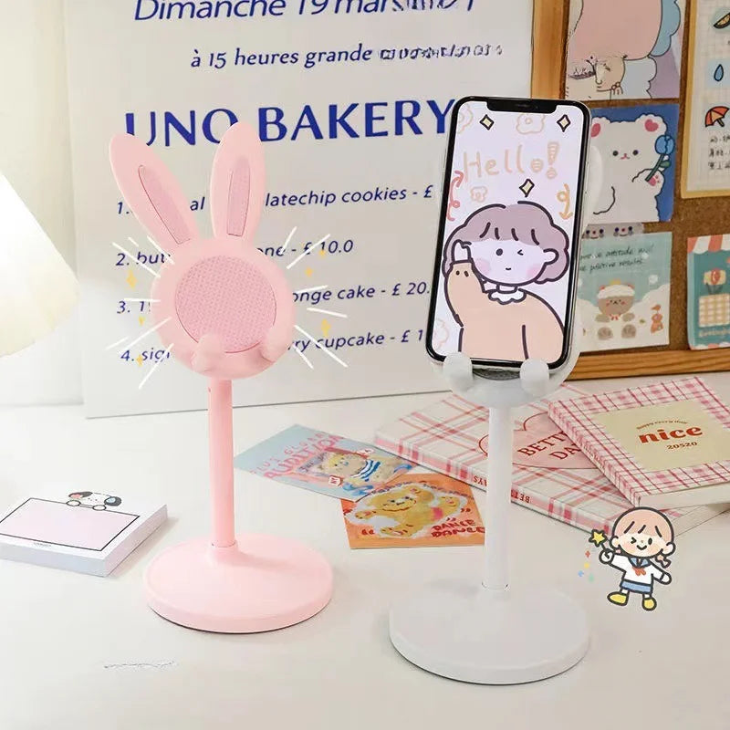 Pink bunny phone stand holding a phone with a cartoon design on a desk.