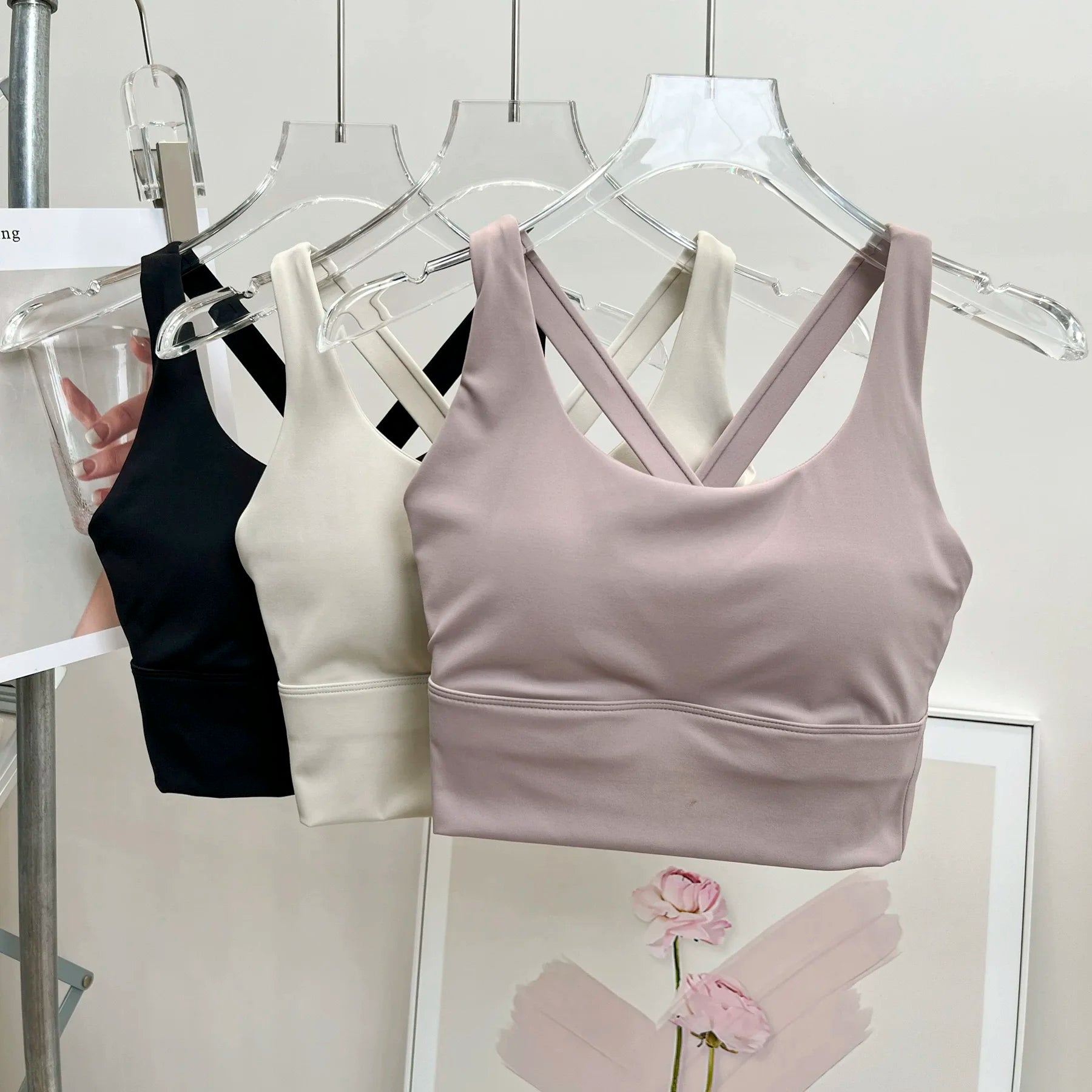 Set of sports bras in black, white, and gray on hangers against a neutral background.