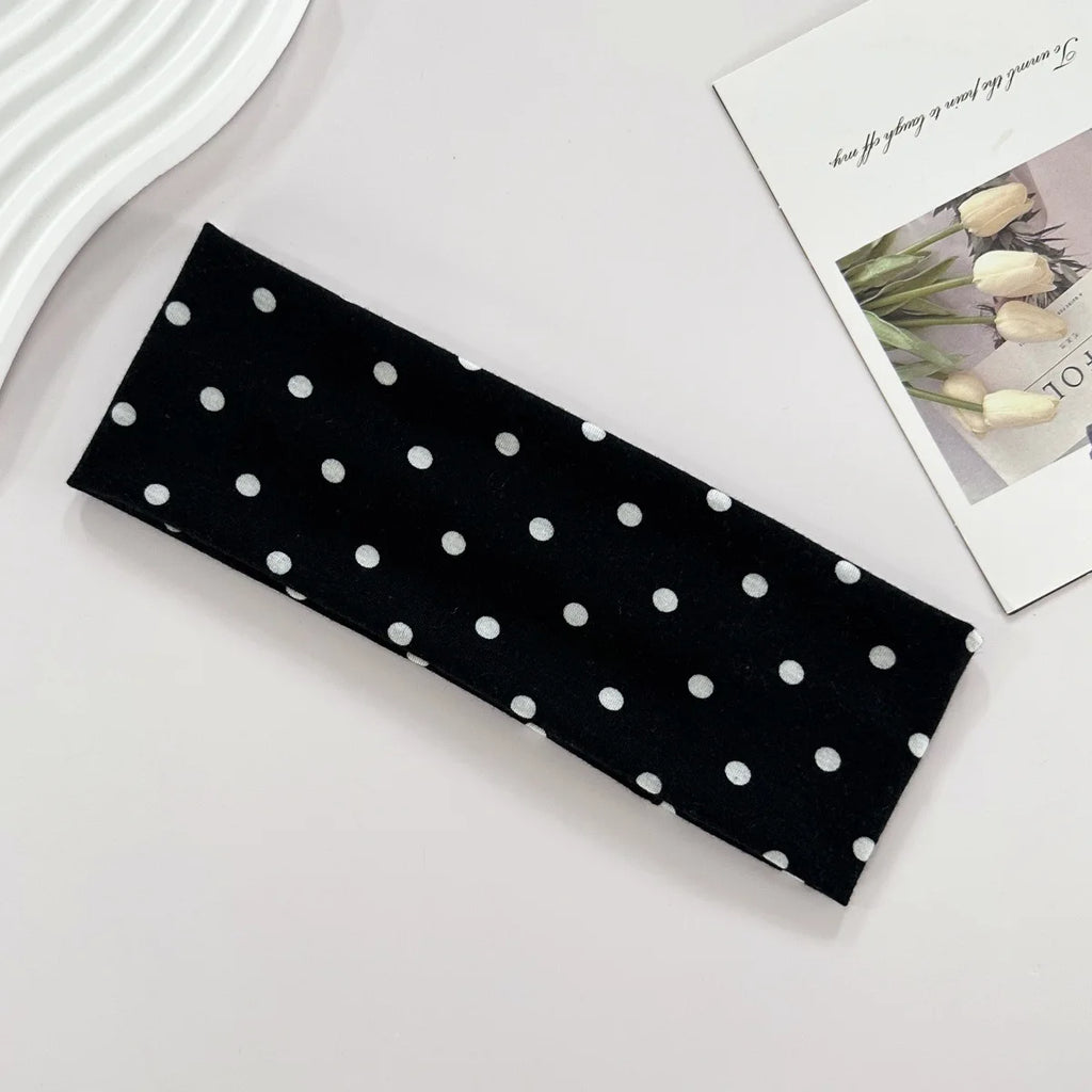 Black headband with white polka dots on a light gray surface